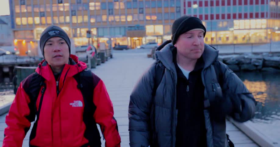 Two men are walking down a pier in a harbor at dusk