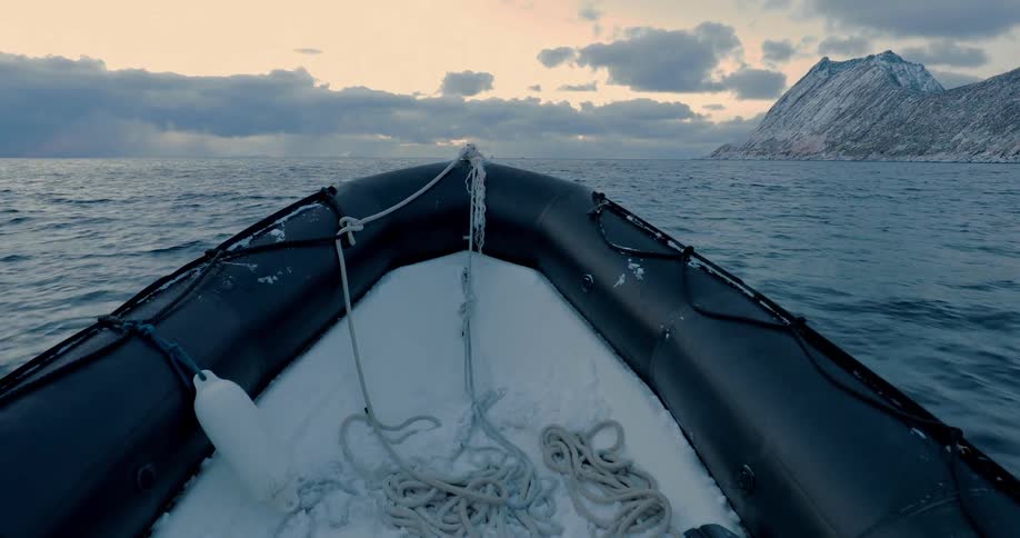 A boat sails through the ocean towards a glacier at sunset with clouds