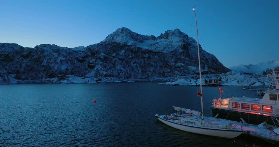 A boat sits docked near snow covered mountains