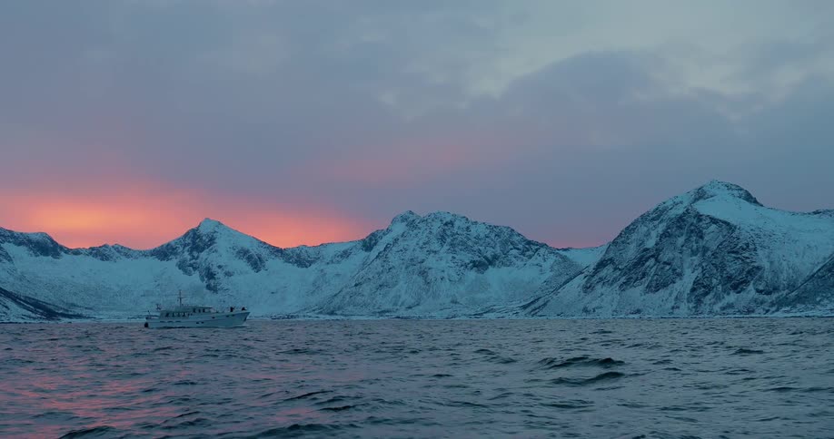 A boat is floating off a snow-covered coastline at dawn