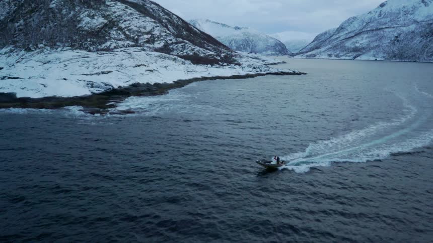 Two people are riding in a dinghy as it speeds along a coastline on a cloudy day
