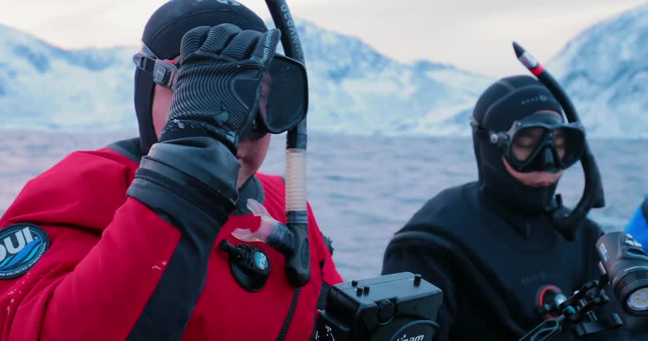 A man is adjusting his diving mask as he sits with another diver on a dinghy