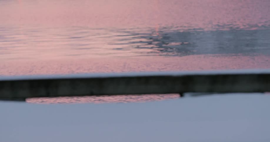 Water ripples next to a snowy dock at sunset