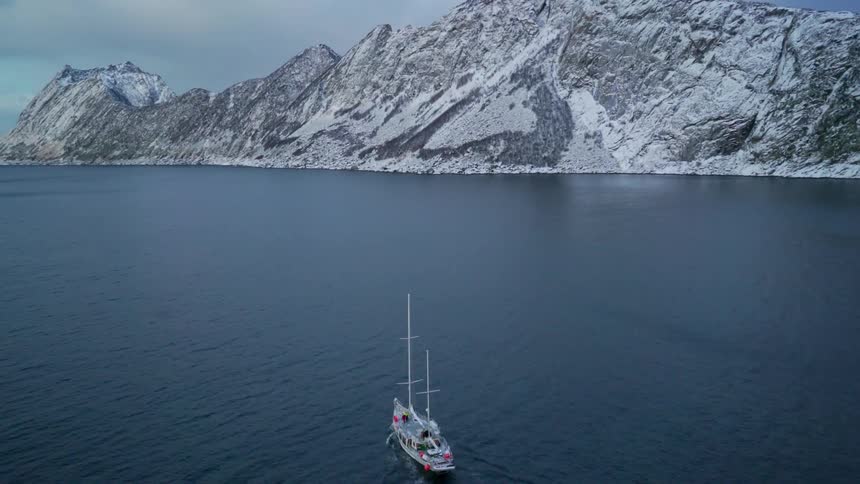Boat moving through the sea with snowy mountains in the background on a cloudy day
