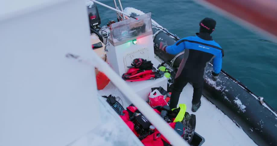 A man in a wet suit inspects gear while on a boat