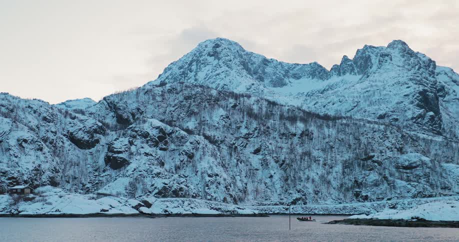 A dinghy is moving away from a mountainous coast on a winter day