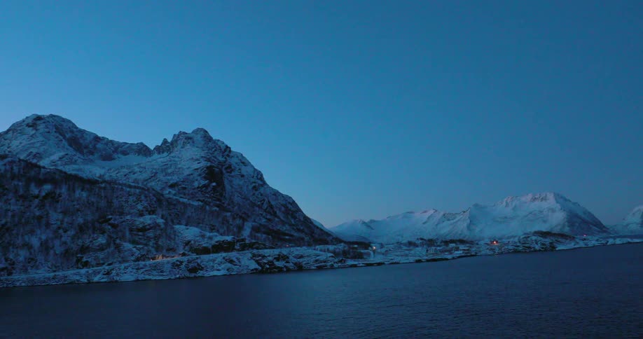 Snowy mountains sit on a coast at dusk