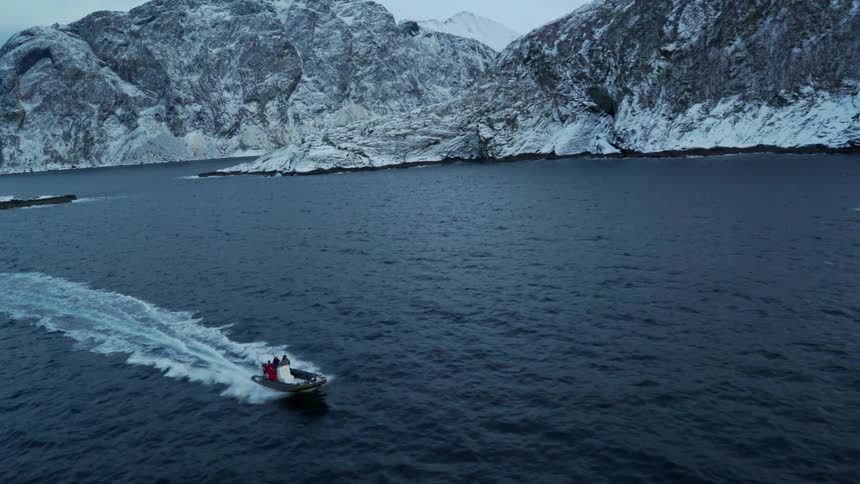 A boat moves quickly through the ocean near the snow covered coast