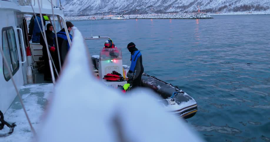 Divers in a raft next to a larger boat on a cold day