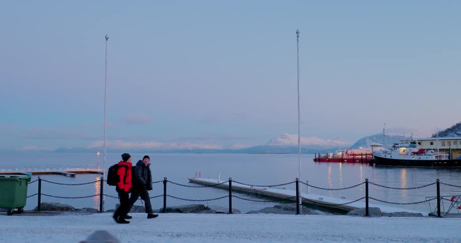 Two people wearing backpacks walk along the harbor in snow