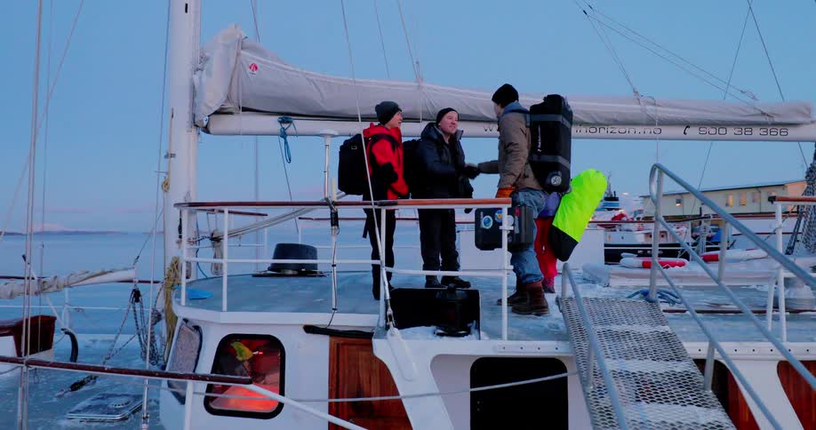 A group of people stand on a boat at port shaking hands and carrying backpacks