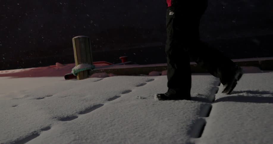 A person walks through the snow on a dock at night