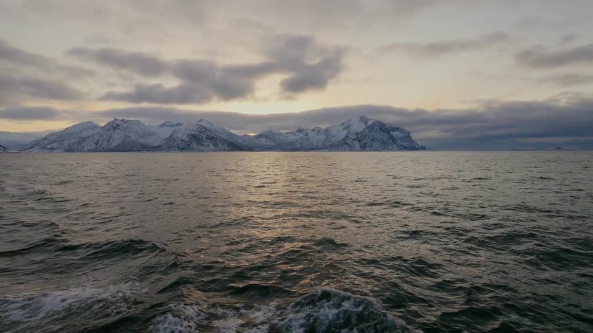 A ship is leaving a wake as it sails away from a coastline at dawn