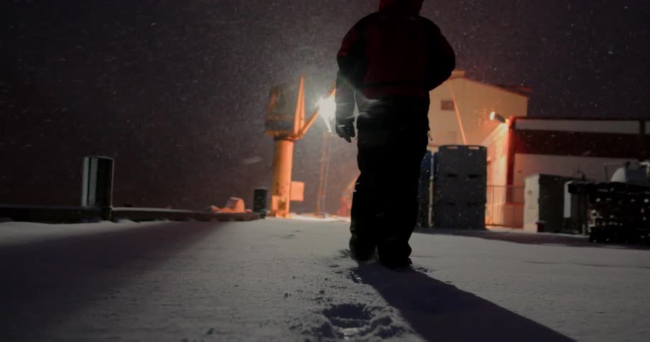 A man is walking through the snow on a dock at night