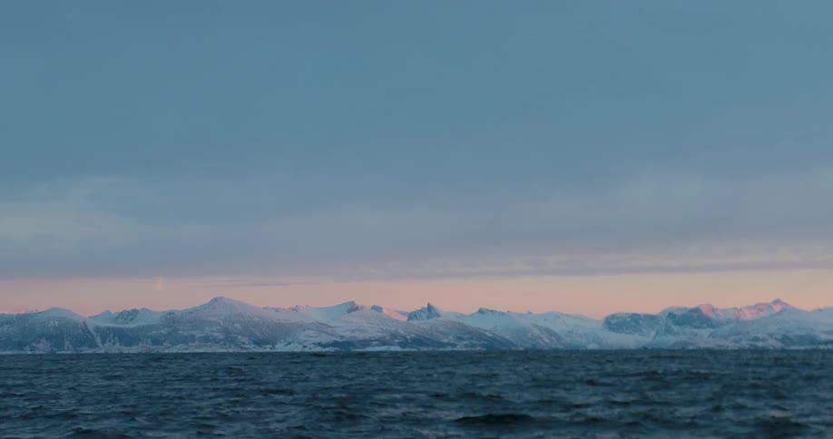 Snowy mountains sit on a shoreline at sunset