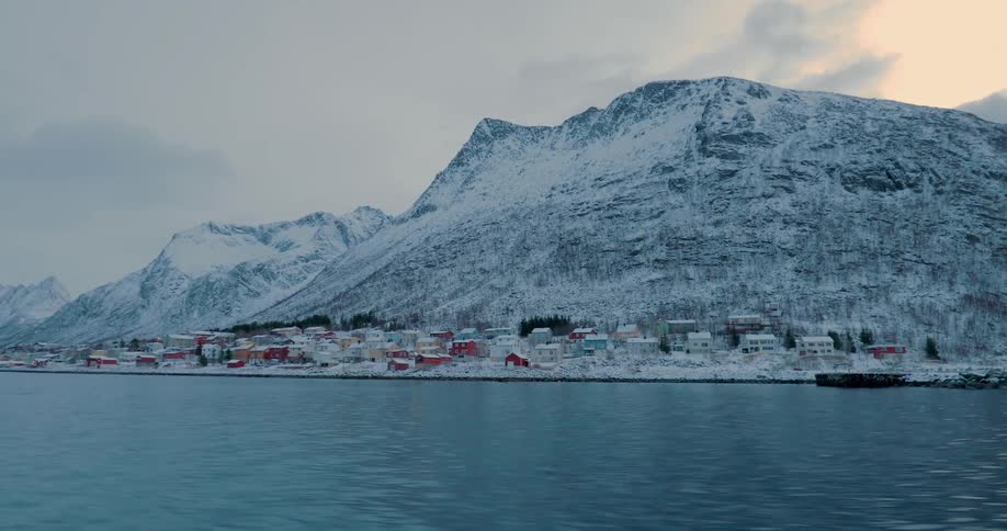 A boat travels past buildings on a snow covered shore
