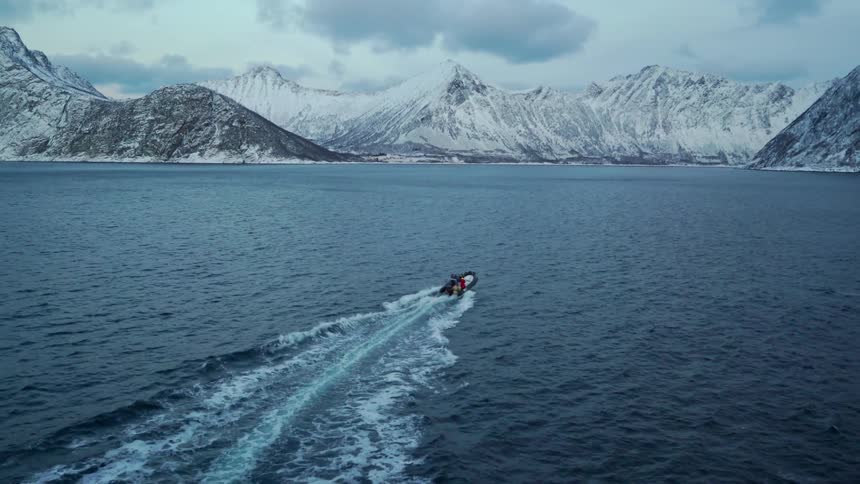 People ride on a small motorized raft in water towards large snowy mountains