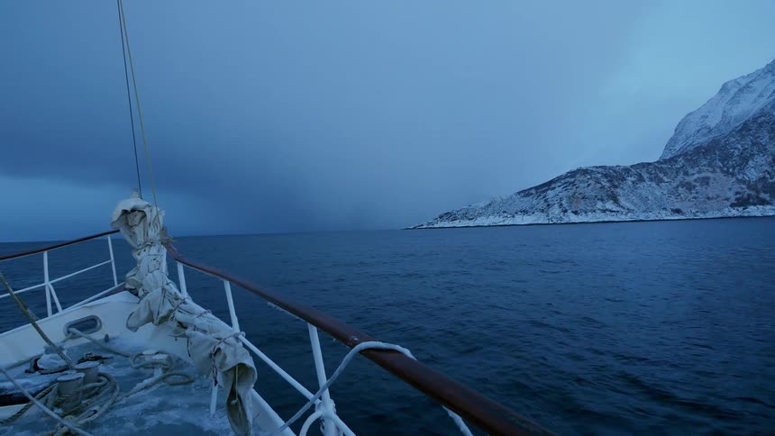 A boat is sailing across a cold lake towards a island covered in snow