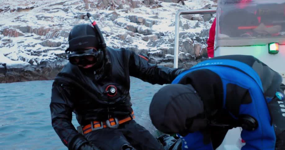 A diver climbs into a raft off a snowy coast