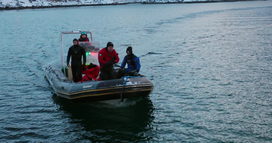 Divers ride in a raft off a snowy coast