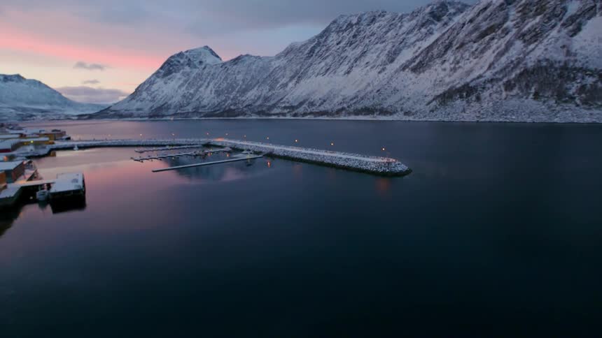 Snow blankets a dock and jetty at a harbor at dawn