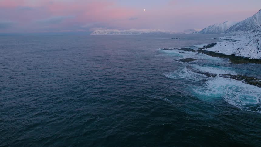 Water crashes into a snowy shoreline at sunrise