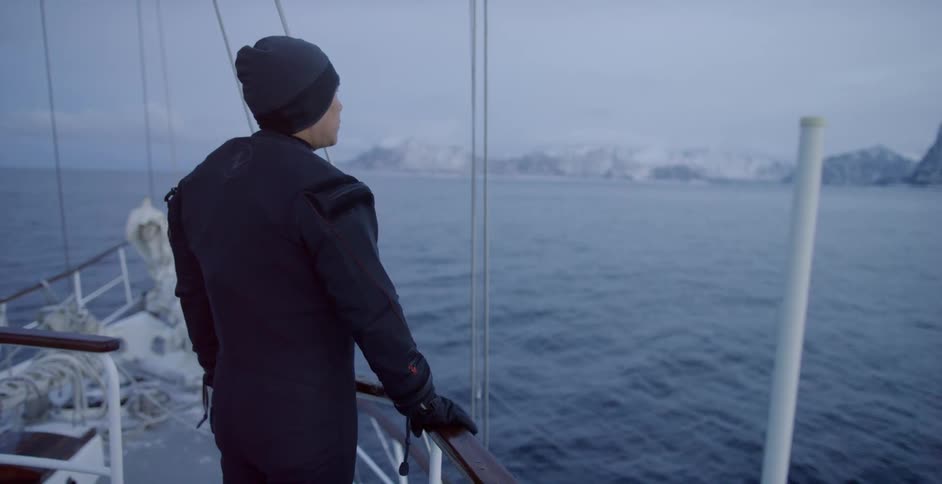 A man stands on a boat and looks out onto the water