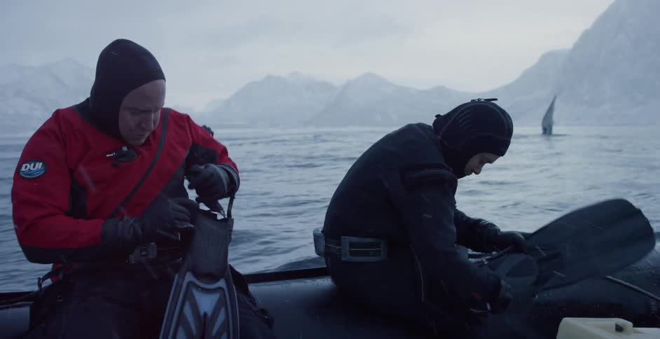 Two men are sitting down in a dinghy to put on their diving fins