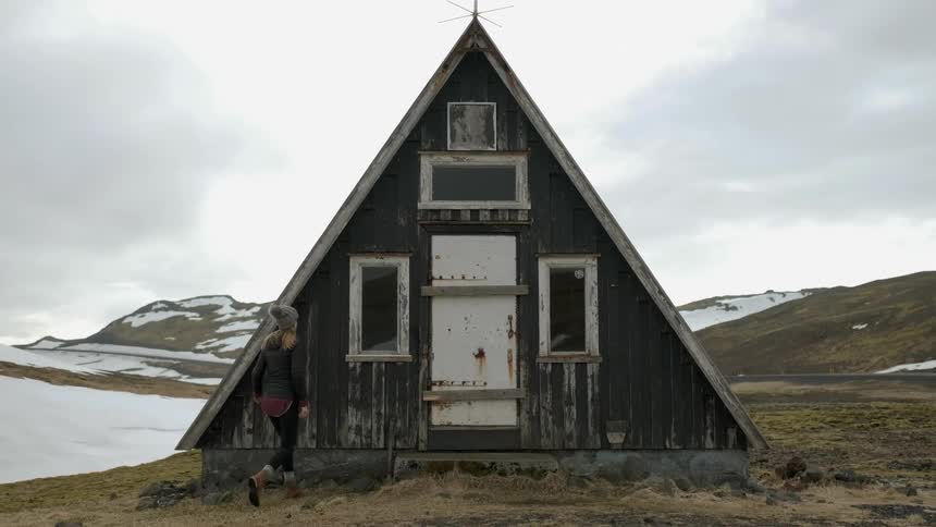 A hiker looks inside a cabin window in the mountains