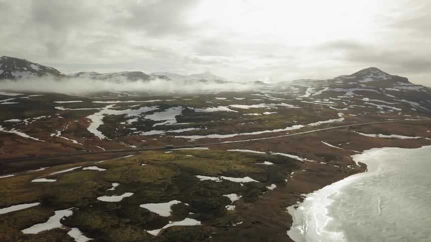 Vehicles travel along a road by the icy shore