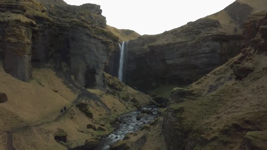 Two people walking in a canyon toward a waterfall