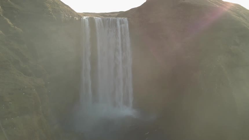 Birds are flying near a waterfall as it is cascading over a cliff during the day