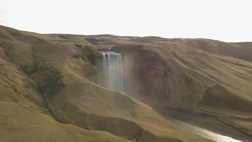 A waterfall is cascading into a river at the bottom of cliffs during the day