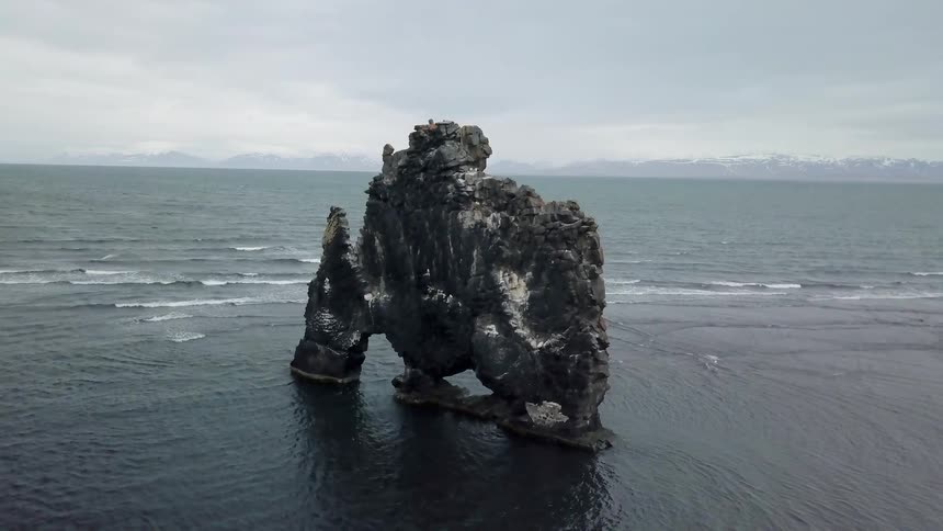 Birds are flying near a rock formation on a beach during the day