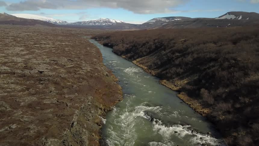 River flowing through some brown grounds on a partly cloudy day