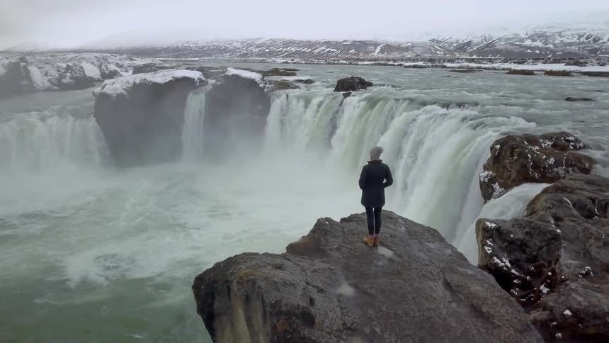 A woman stands on the cliff looking out onto the water