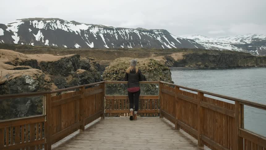 A woman is walking to the end of a wooden path to take in a view during the day