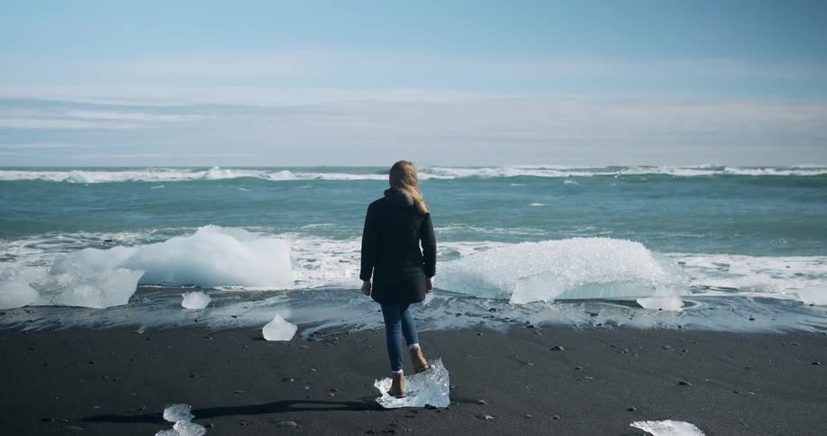 A woman stands on a piece of ice on the beach
