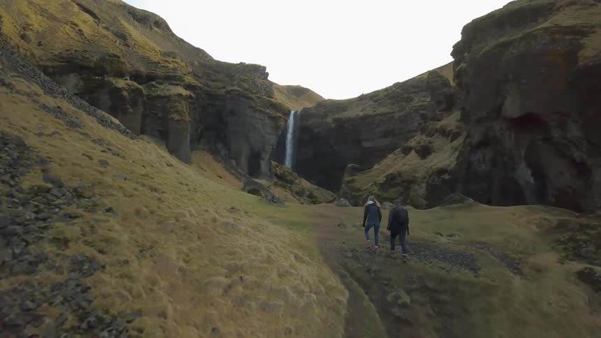 Two people hike up a hill towards a waterfall