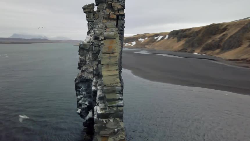 Water flows between a tall rock formation by the shore