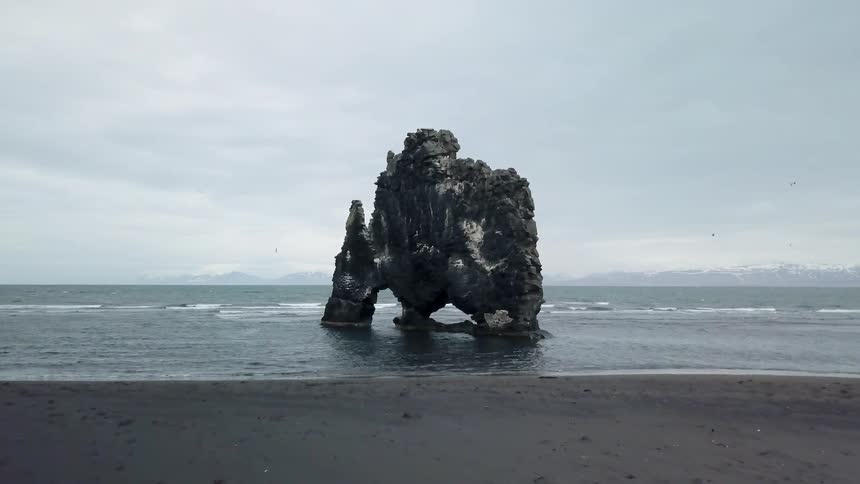 Birds are flying near a rock formation on a beach during the day