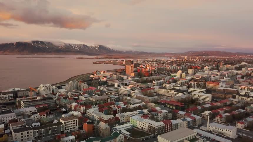 A city with a large body of water that has mountains on the opposite side with clouds in the sky