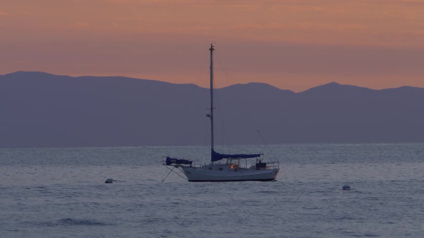 A sailboat is on a lake near mountains at dusk