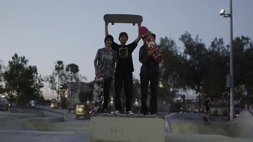 Teenagers hold up skateboards in a skatepark at dusk