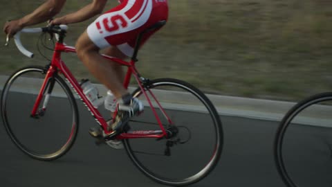 Professional cyclists ride in a single-file formation on an asphalt road