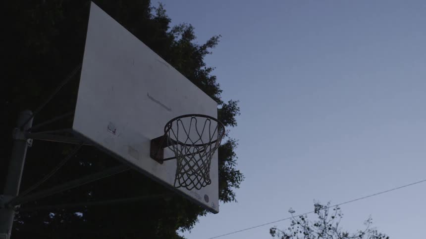 A basketball hoop hangs in a park at dusk