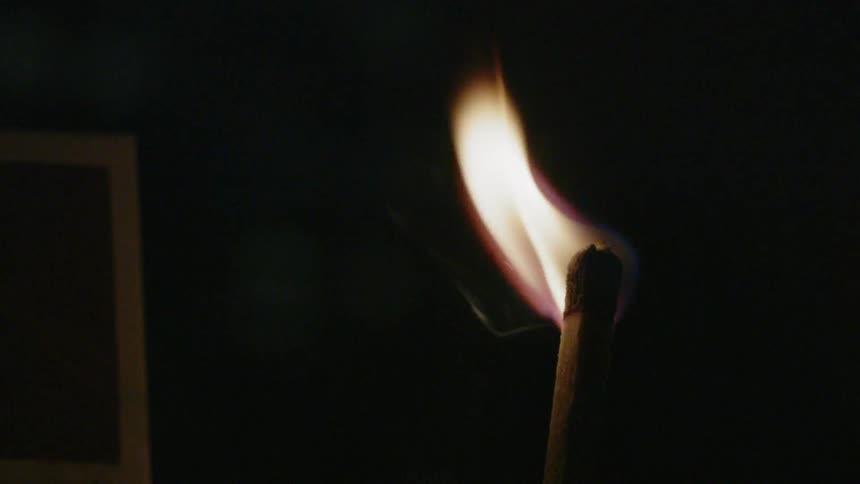 A flame is burning on the end of a matchstick in a dark room