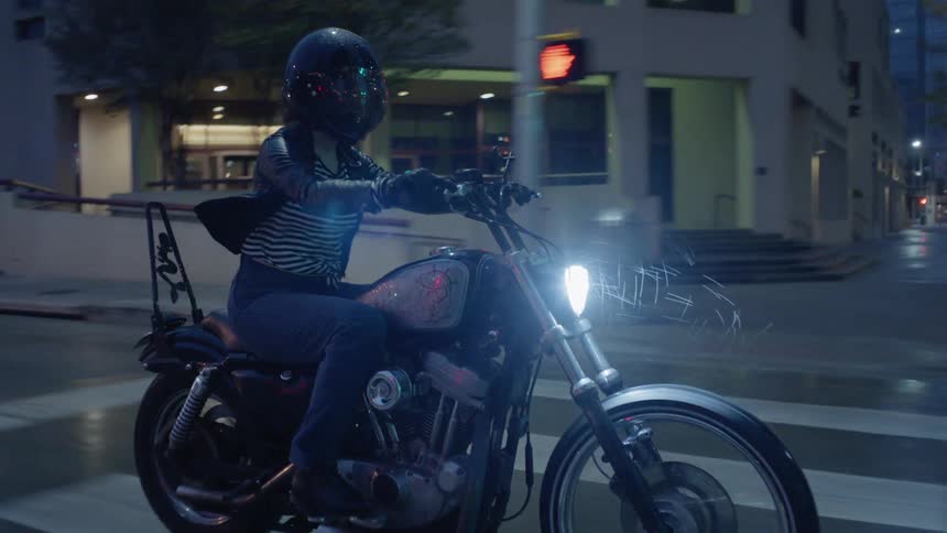 A woman is riding a motorcycle on a city street at dusk in the rain