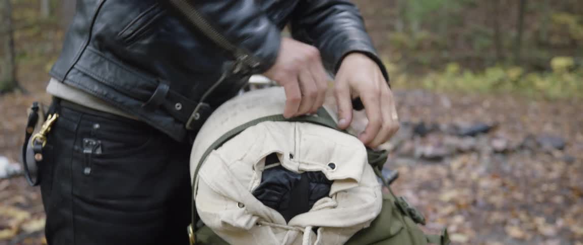 Man unfastens duffel bag from motorcycle in the woods