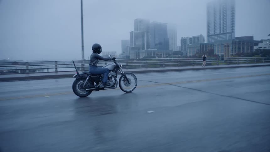A motorcyclist rides on a city bridge while it rains
